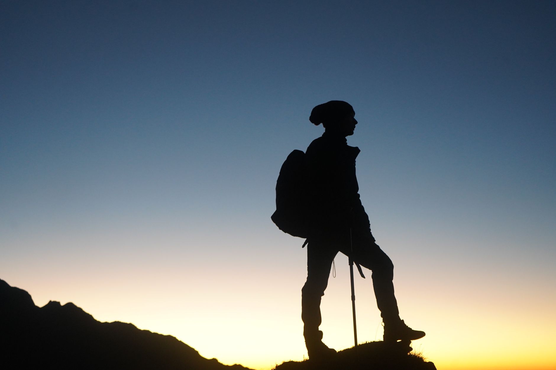 A lone hiker stands silhouetted against a stunning sunrise sky on a mountain trail