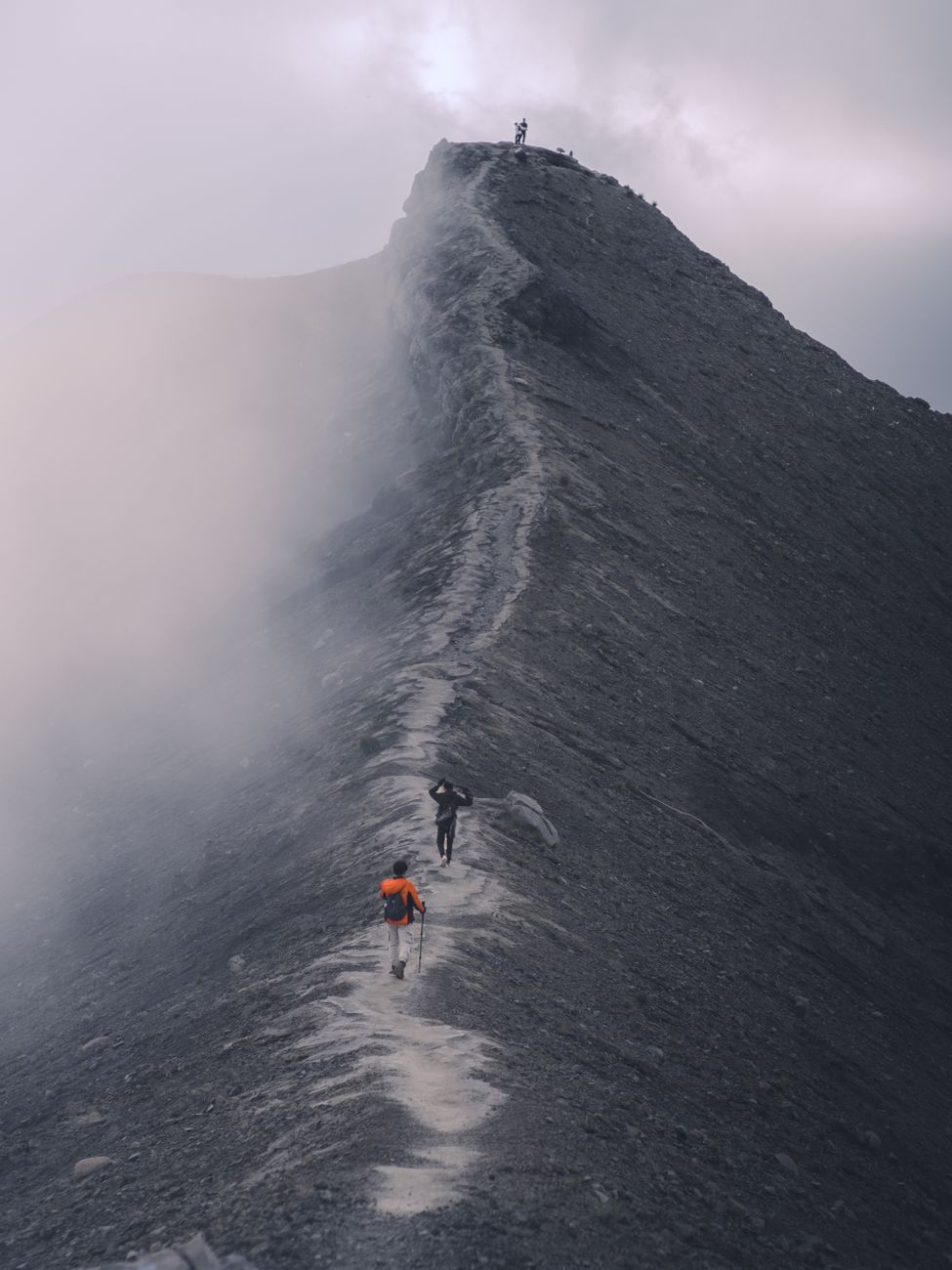 Hikers traverse a dramatic mist-covered mountain ridge