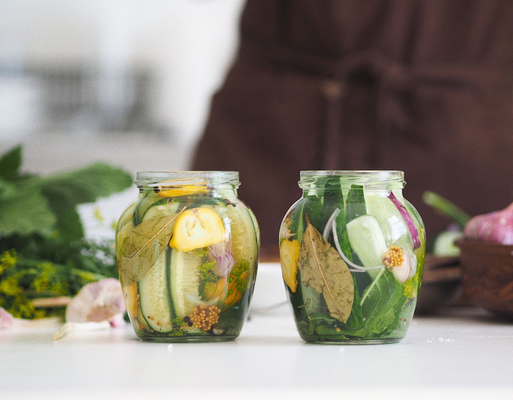 Two glass jars filled with homemade pickled cucumbers and herbs