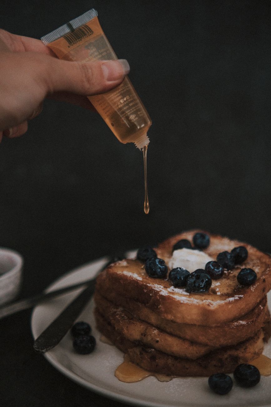 A person drizzling honey on top of breakfast pancakes