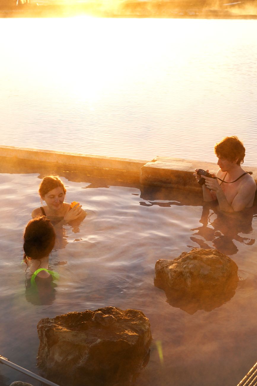 Three adults enjoying a peaceful soak in a hot spring at sunset