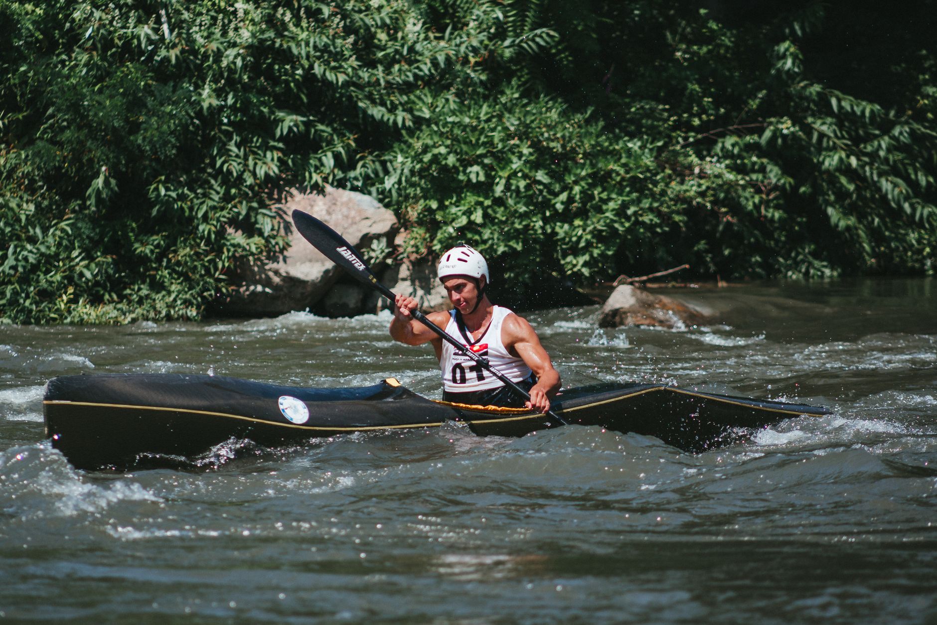 A man skillfully navigating a kayak through river rapids amid lush greenery