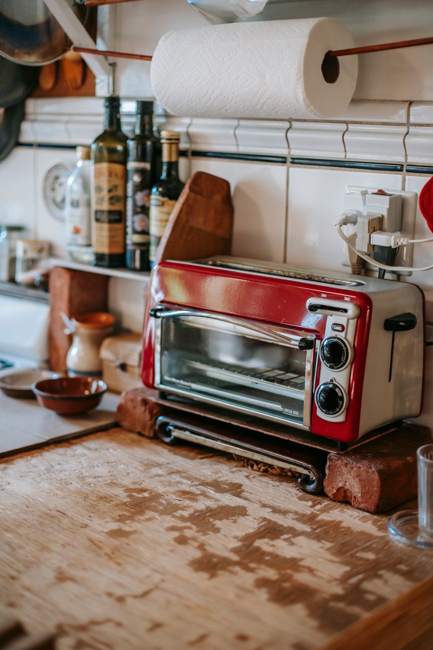 Part of a kitchen with paper towels and a toaster oven standing on a shelf