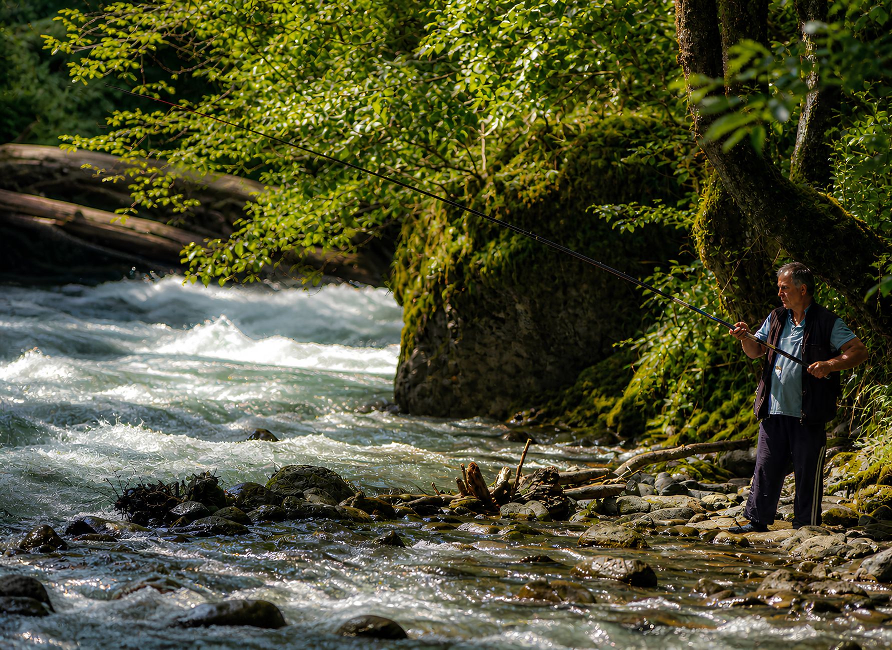 A man fishing by a rushing mountain stream surrounded by lush greenery