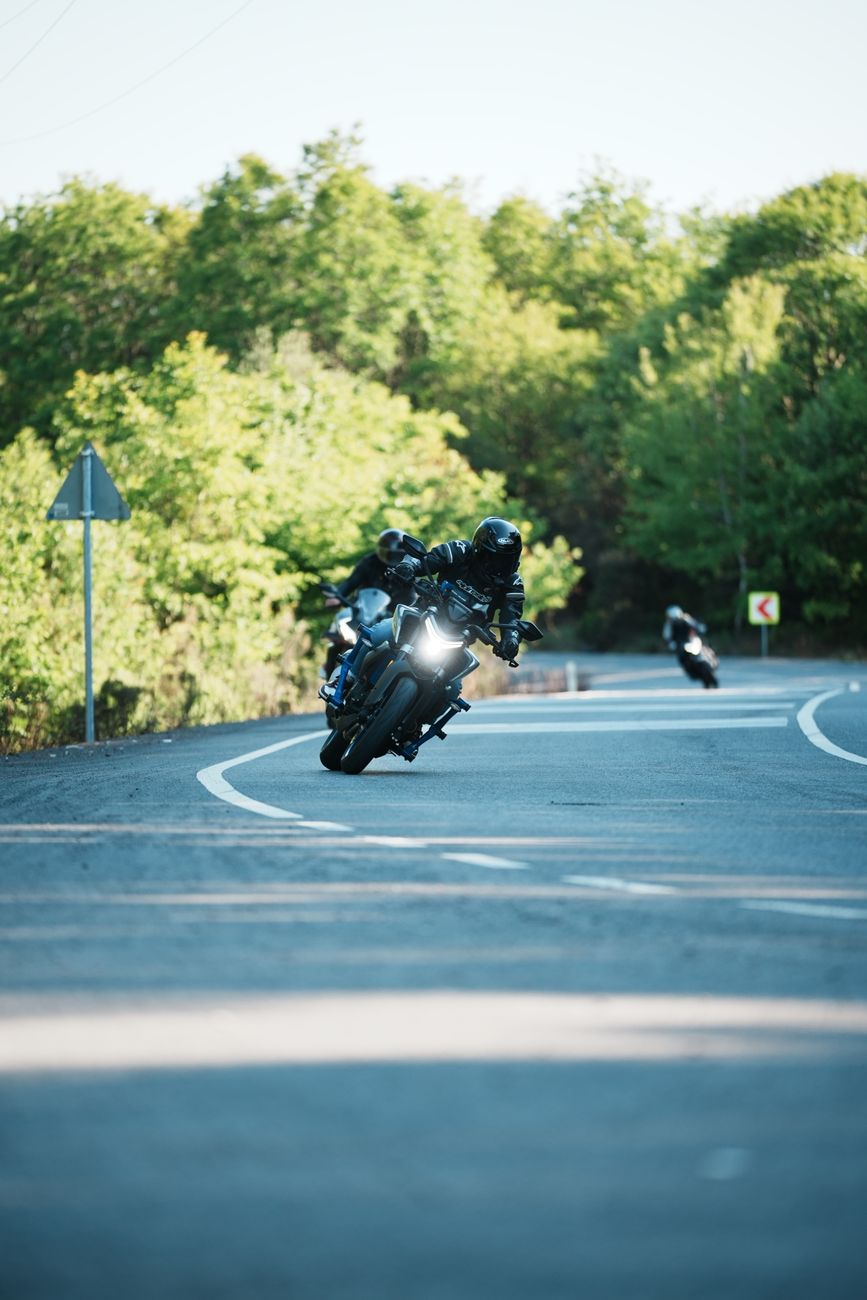 Two motorcyclists navigating a scenic curved road surrounded by lush greenery