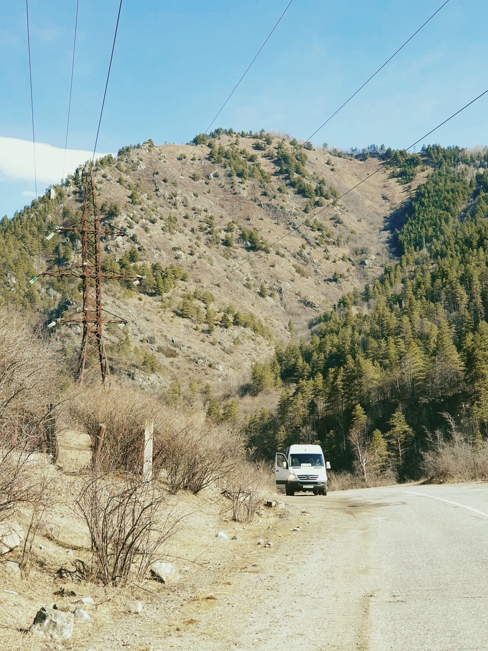 Serene mountain road with a vehicle, surrounded by nature and power lines