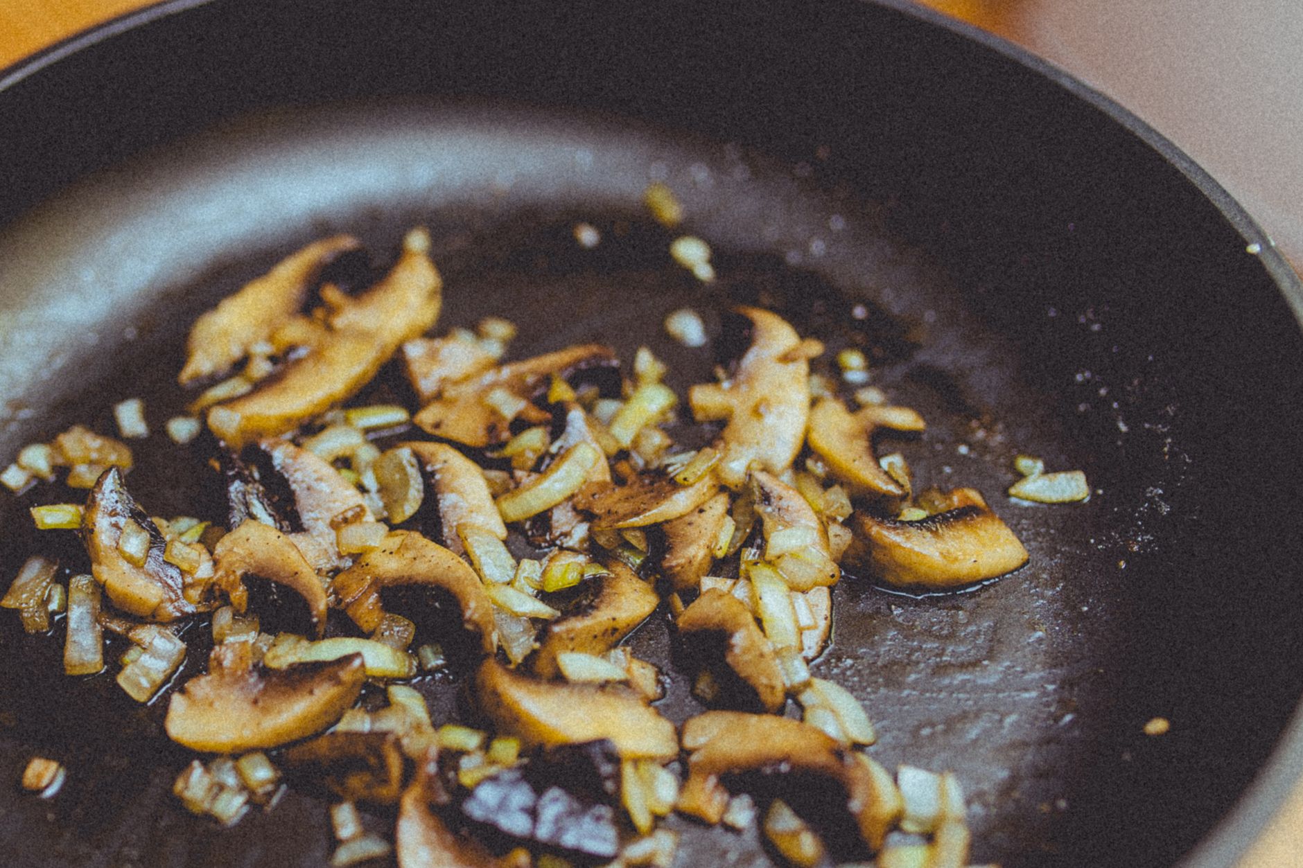 Close-up of sliced mushrooms and onions sauteing in a skillet