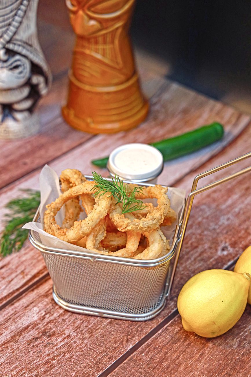 A basket filled with onion rings and fresh lemon wedges