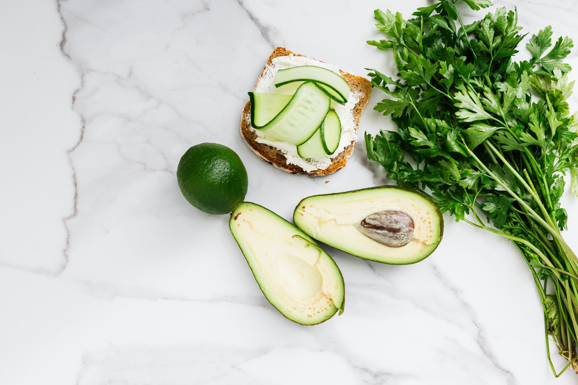 An open sandwich with avocado, cucumber, parsley, and cream cheese