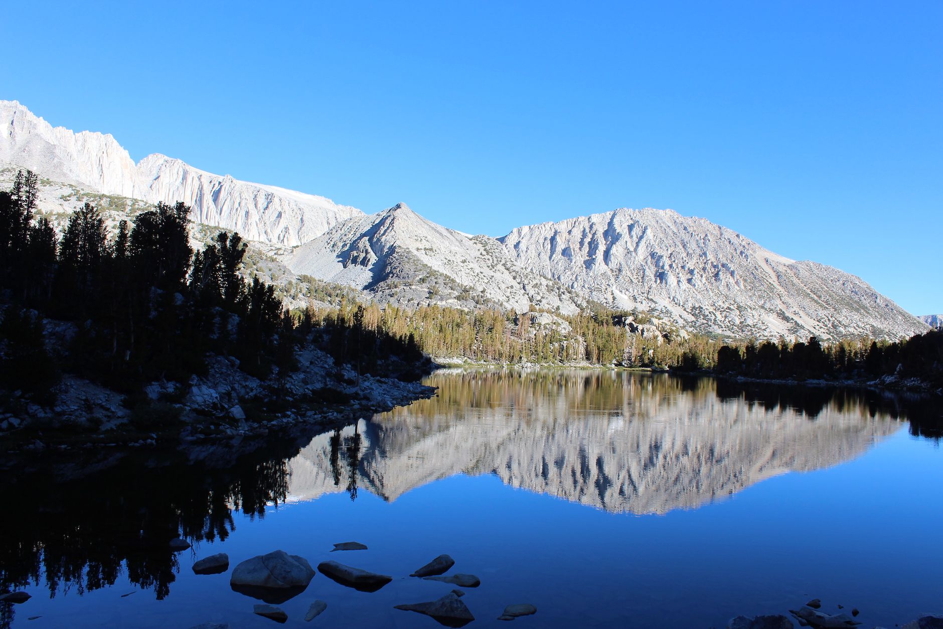 A peaceful mountain landscape with lake reflections under a clear blue sky