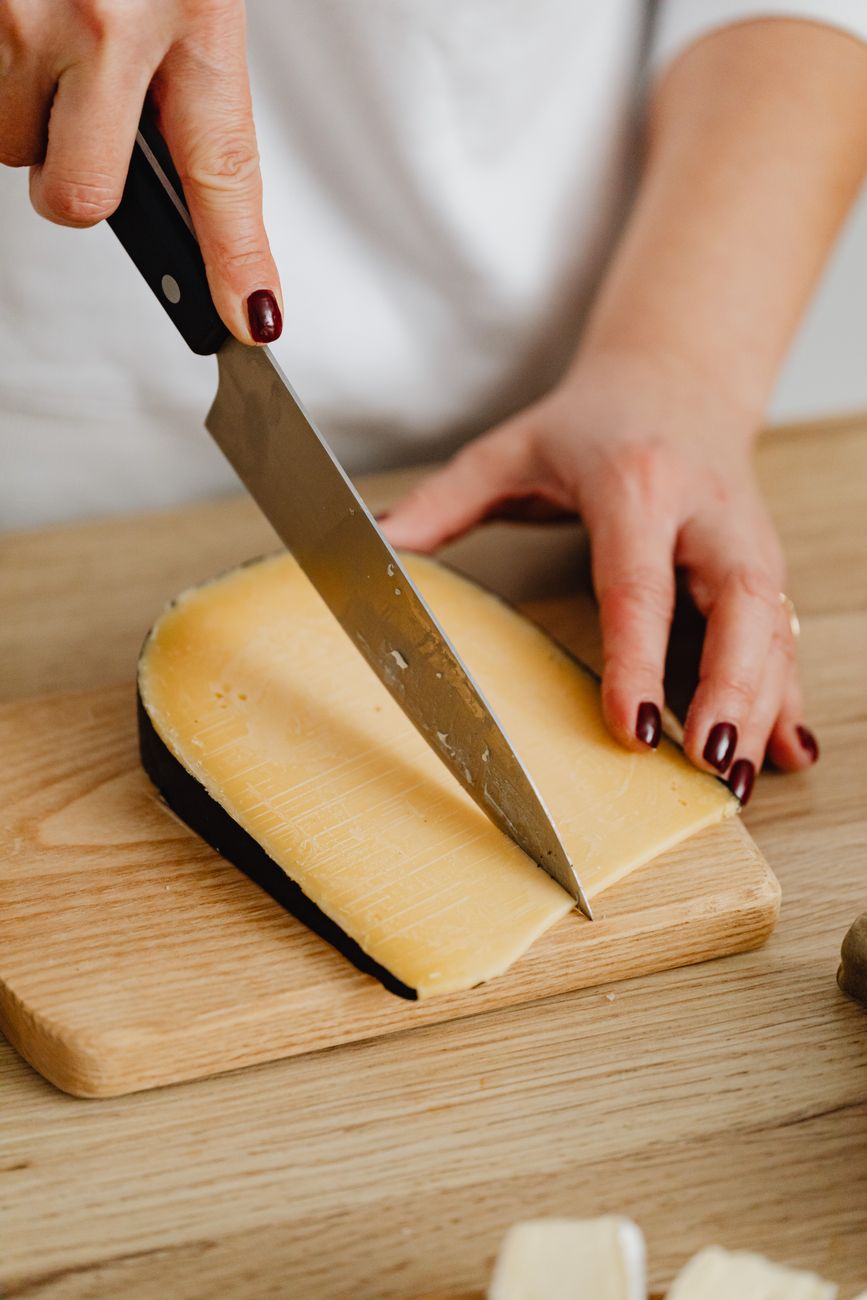A person delicately slices cheese on a wooden board with a sharp knife