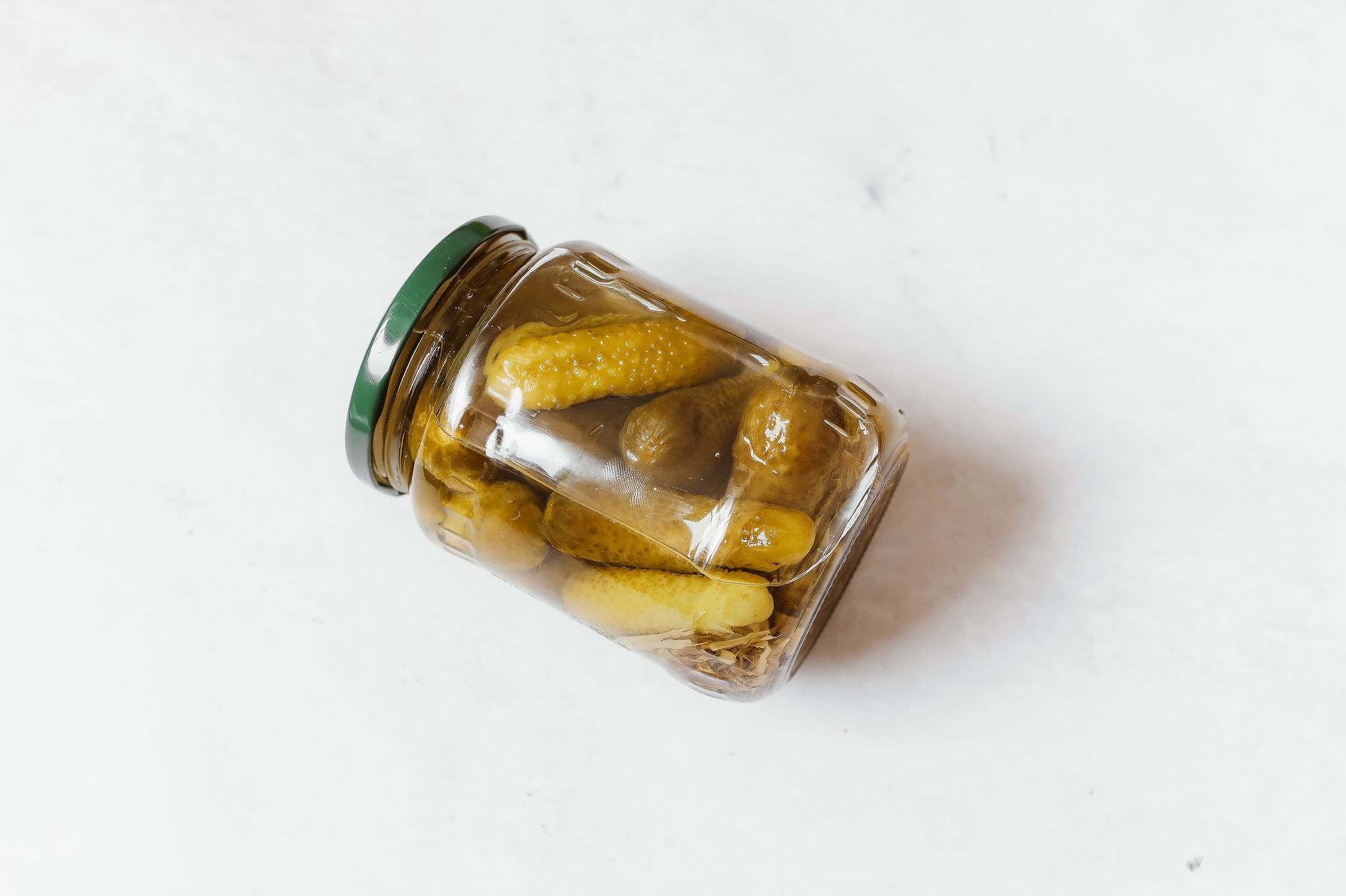 Glass jar with pickled cucumbers on a white surface