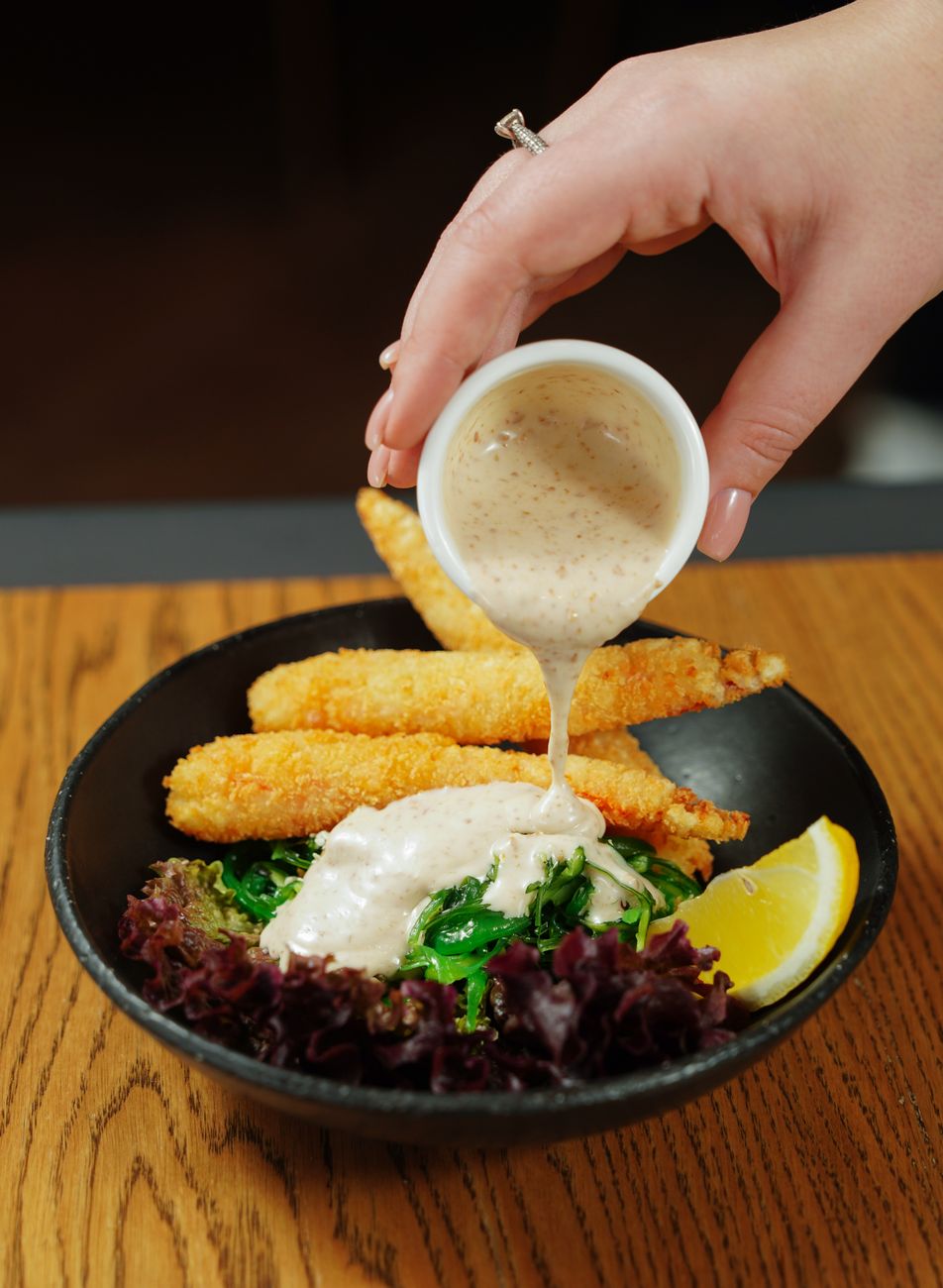 Close-up of hand pouring creamy sauce over crispy chicken strips
