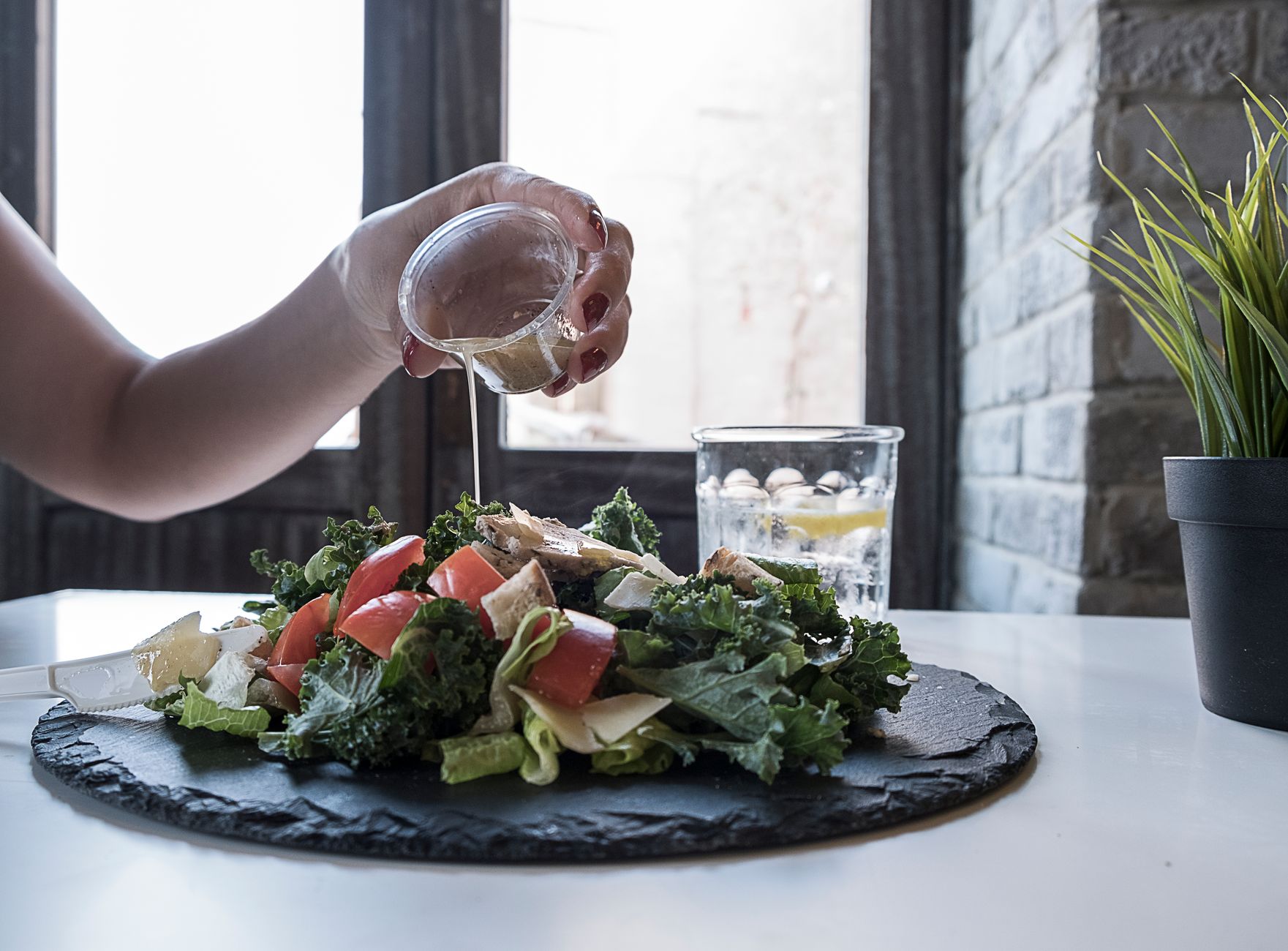 Hand pouring dressing over fresh salad with kale and tomatoes