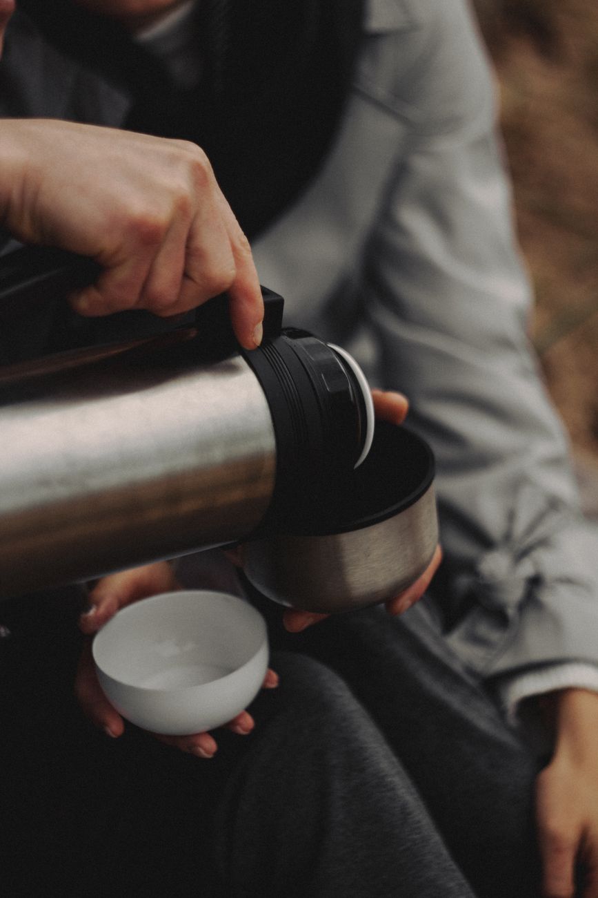 A person pouring a hot beverage into a cup from a thermos