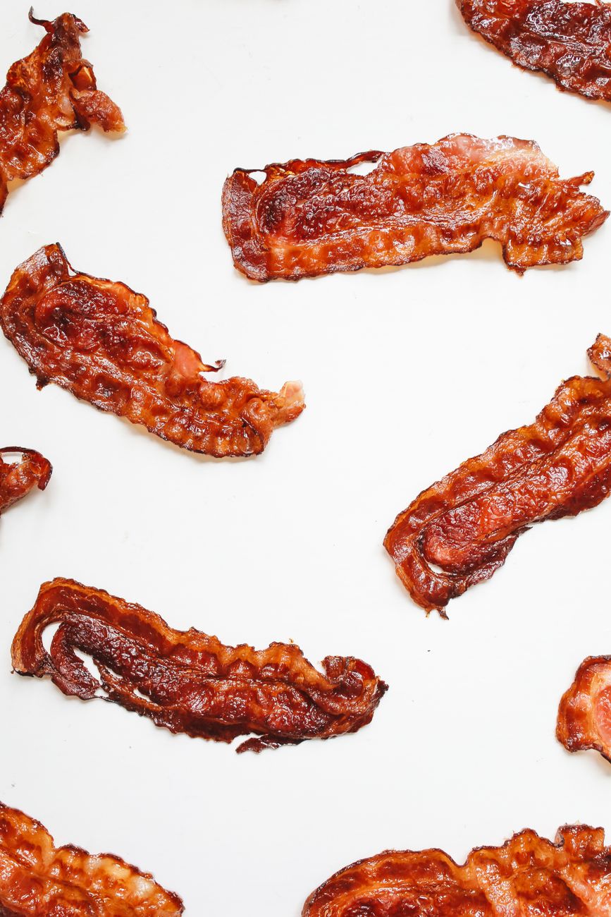 Raw brown bacon strips laid out on a white surface