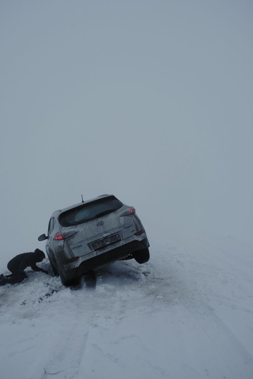 A person trying to rescue a car stuck in snow on a cold winter day