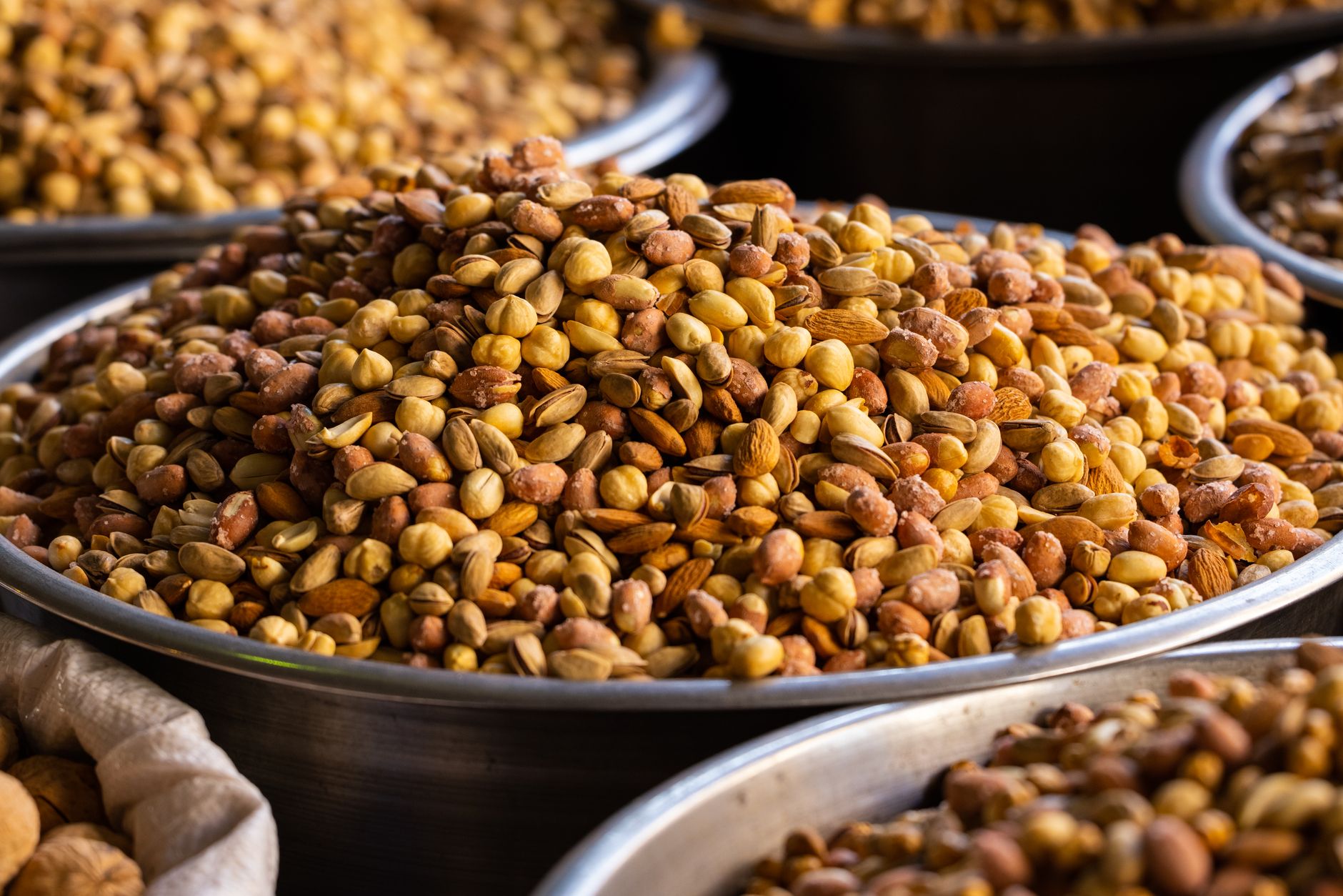 A close-up of assorted roasted nuts in stainless steel bowls