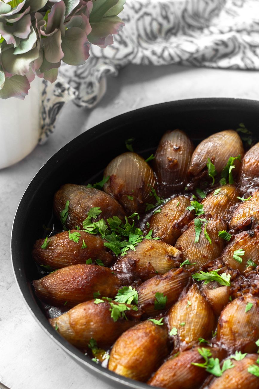Close-up of roasted shallots in a frying pan garnished with fresh herbs