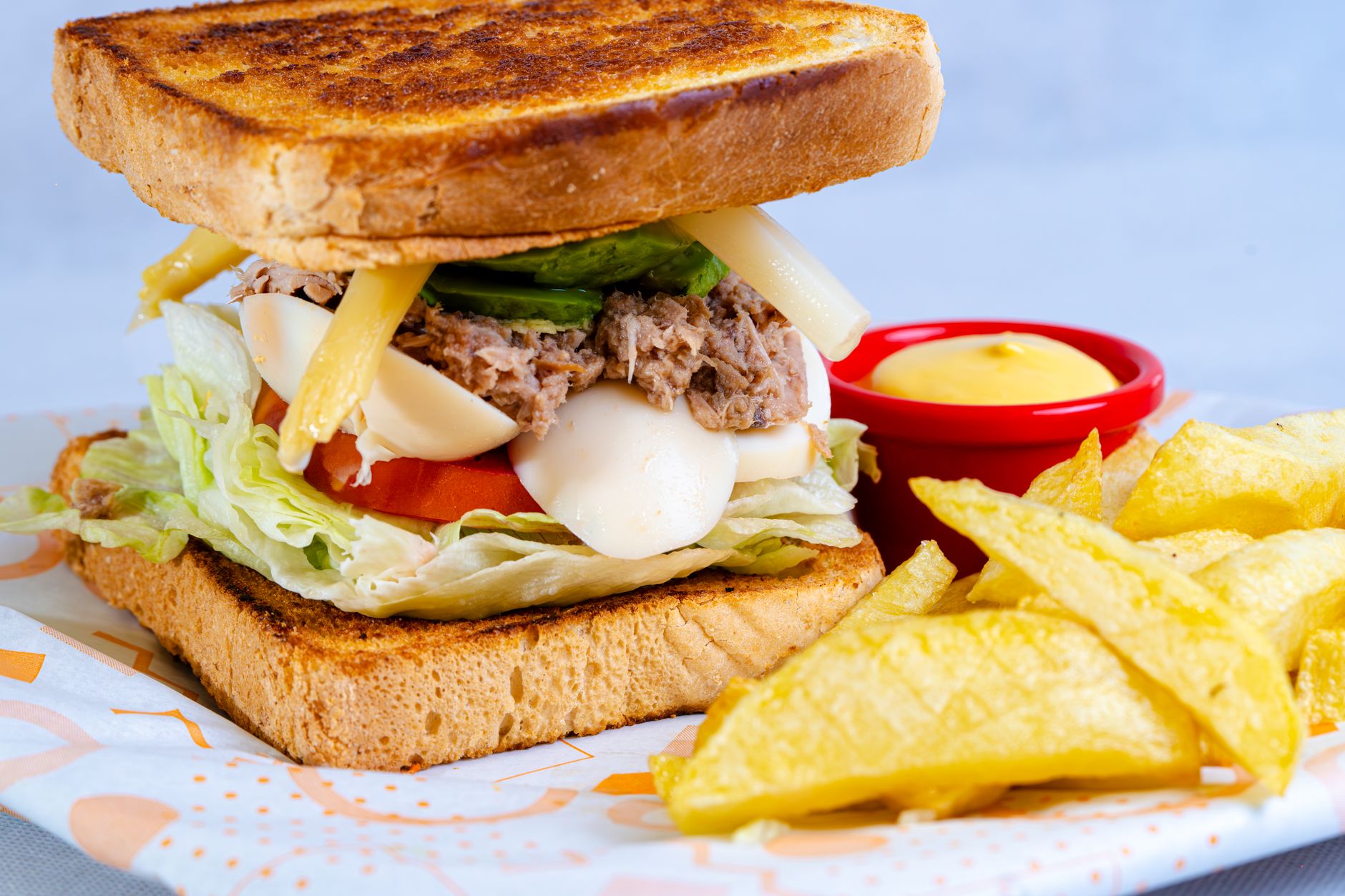 A sandwich with cheese, lettuce, and tomato served with fries