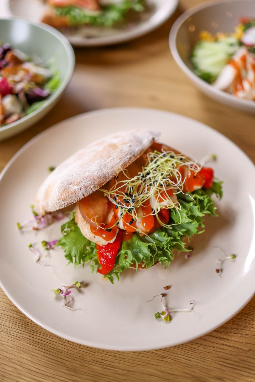 A sandwich served on a plate with salad and fresh vegetables