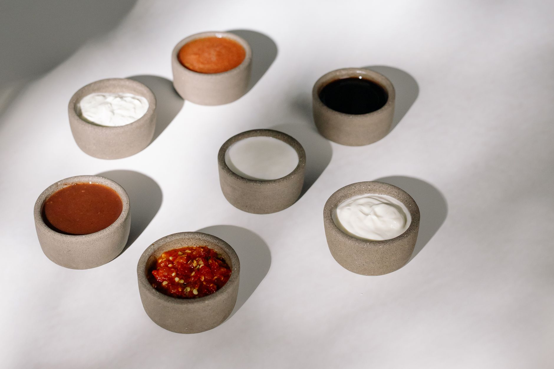 Variety of sauces and dips in rustic ceramic bowls under natural sunlight