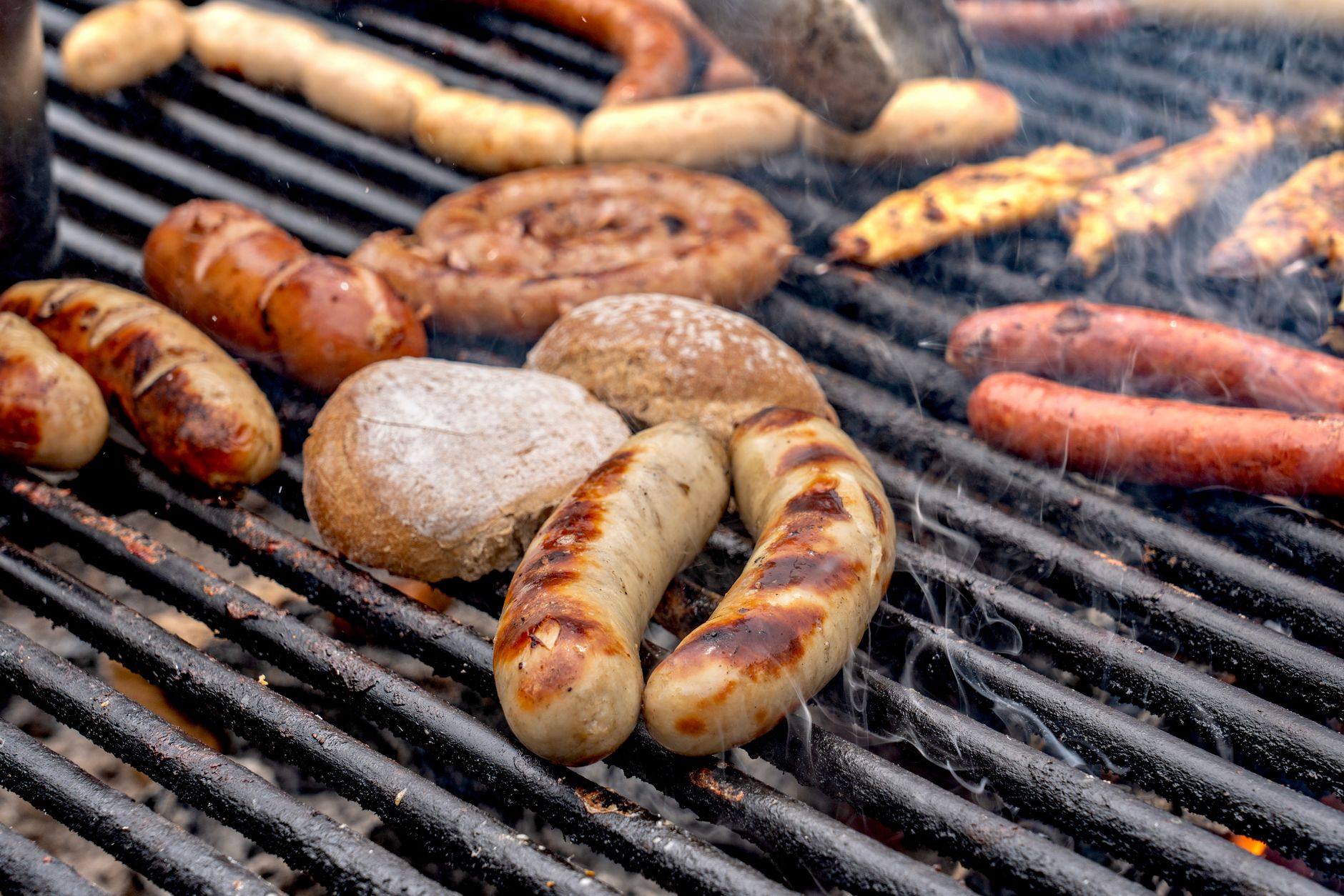 A close-up view of various sausages and bread grilling on a barbecue