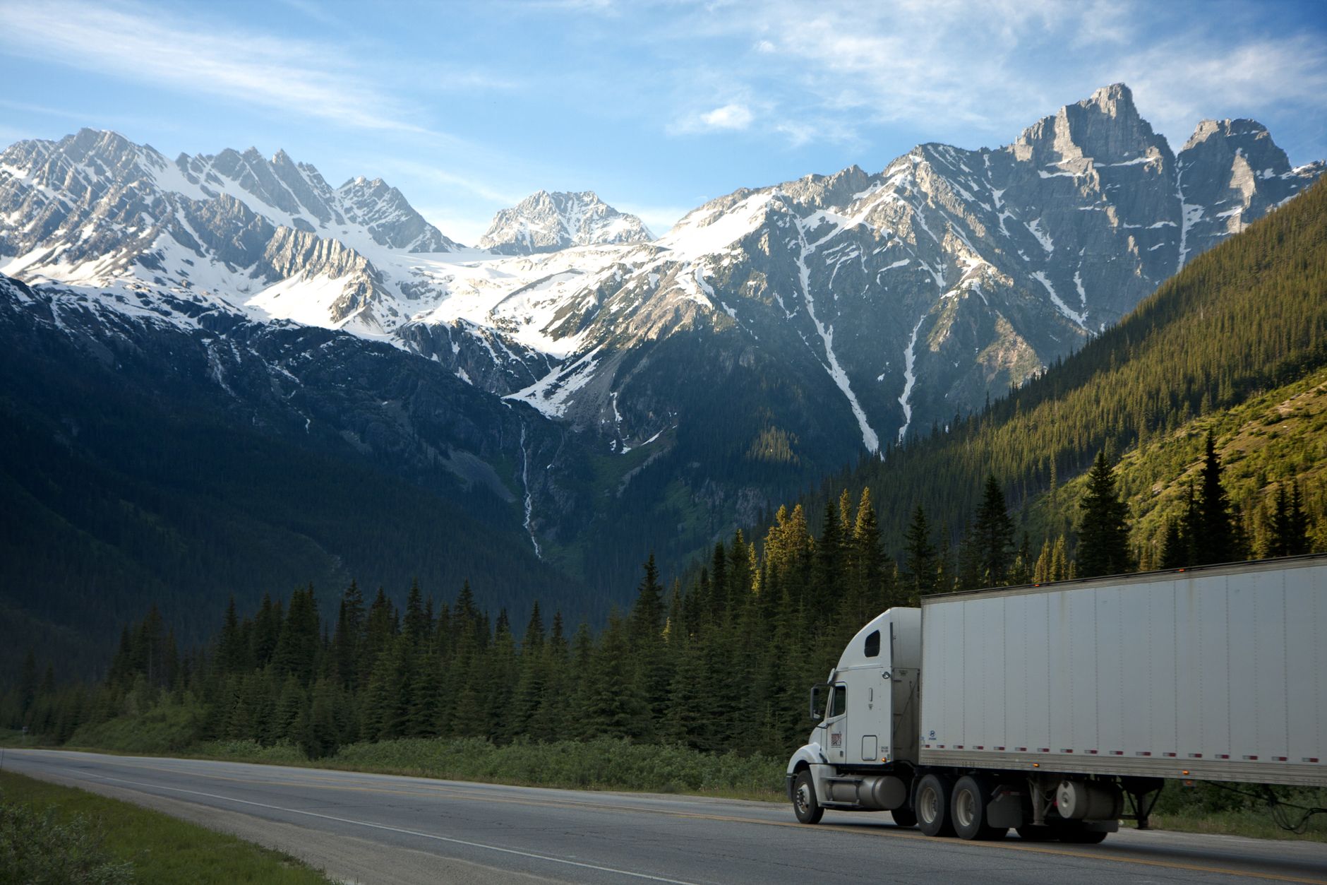 Semi-truck driving a highway with snow-capped mountains in the background