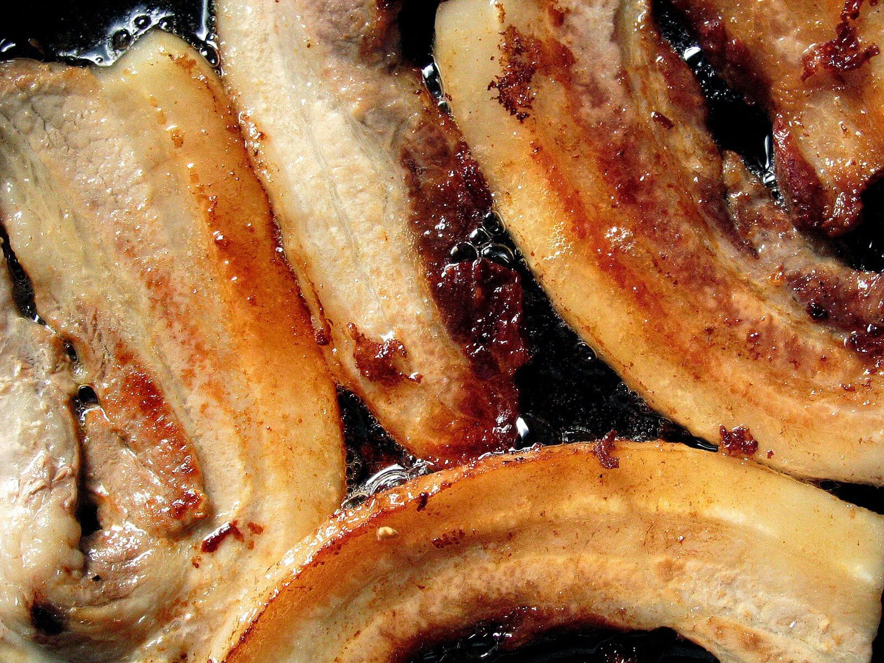 A close-up of sizzling bacon strips cooking in a frying pan