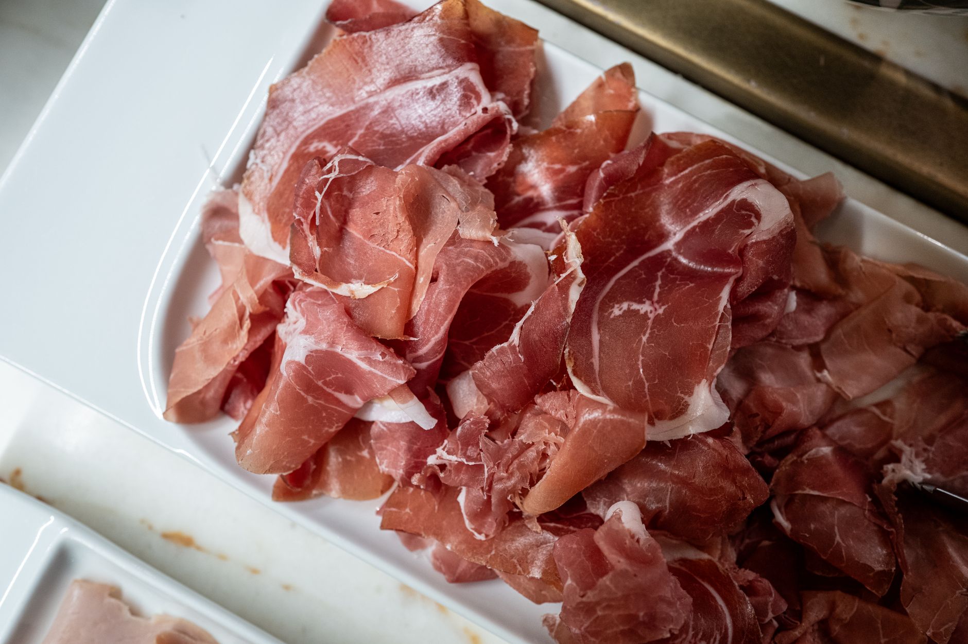 Freshly sliced prosciutto ham served on a white tray in the kitchen