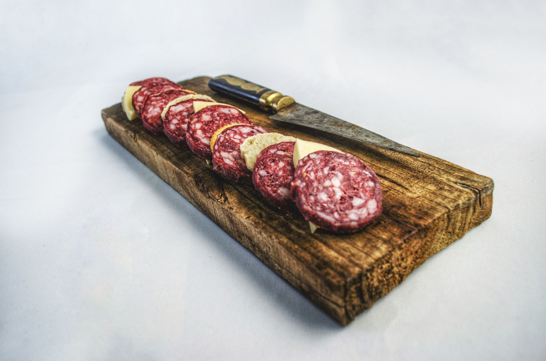 A rustic wooden board displaying sliced salami and a knife
