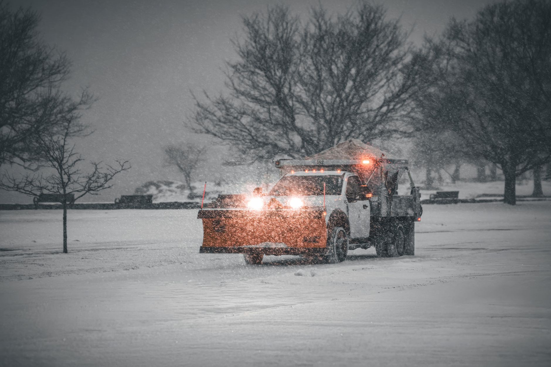 A snow plow truck clearing a snowy road during a winter storm