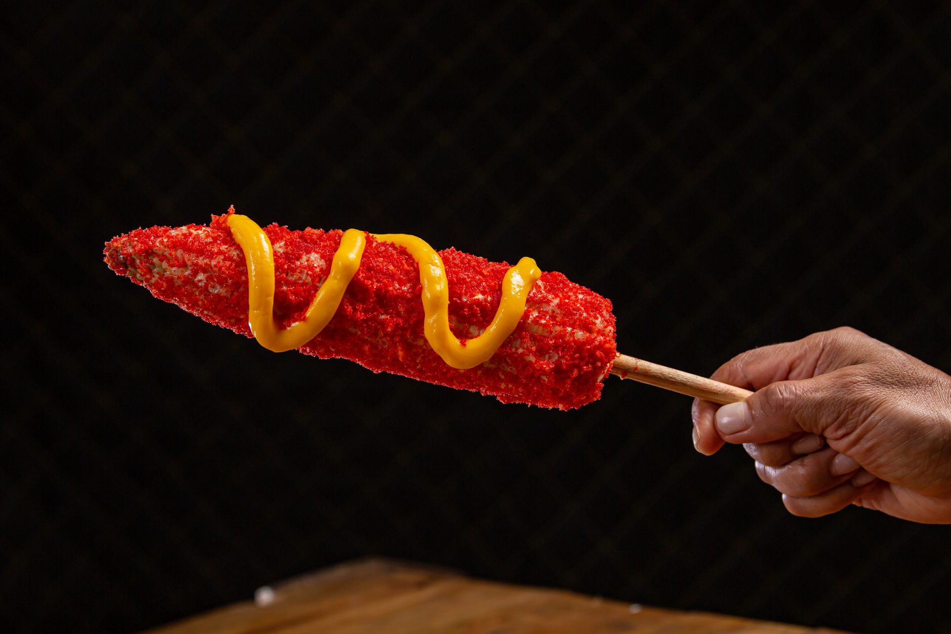 Close-up of a spicy corn dog topped with cheese held in hand