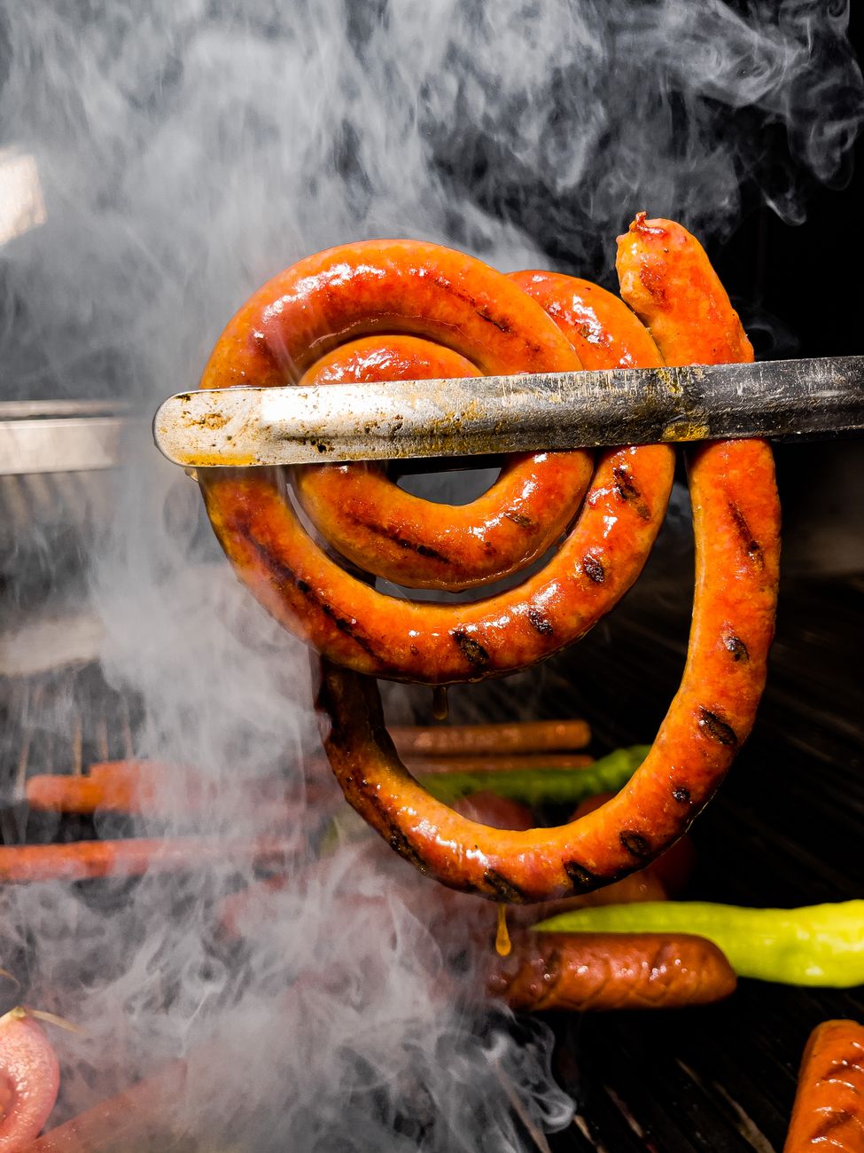Close-up of a spiral sausage being grilled, captured in a smoky atmosphere