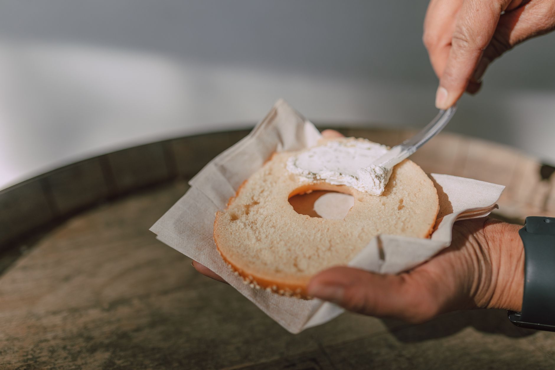 A person spreading cream cheese onto a fresh bagel