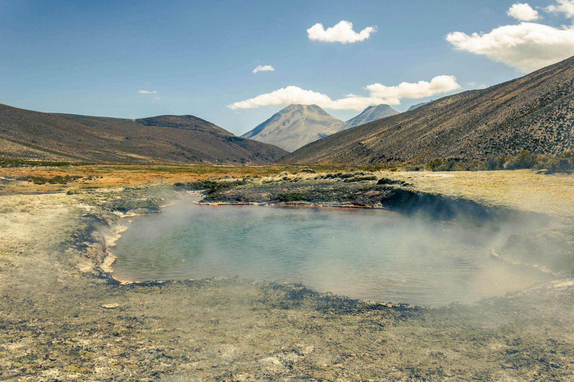 A steaming natural hot spring set against a dramatic mountain landscape