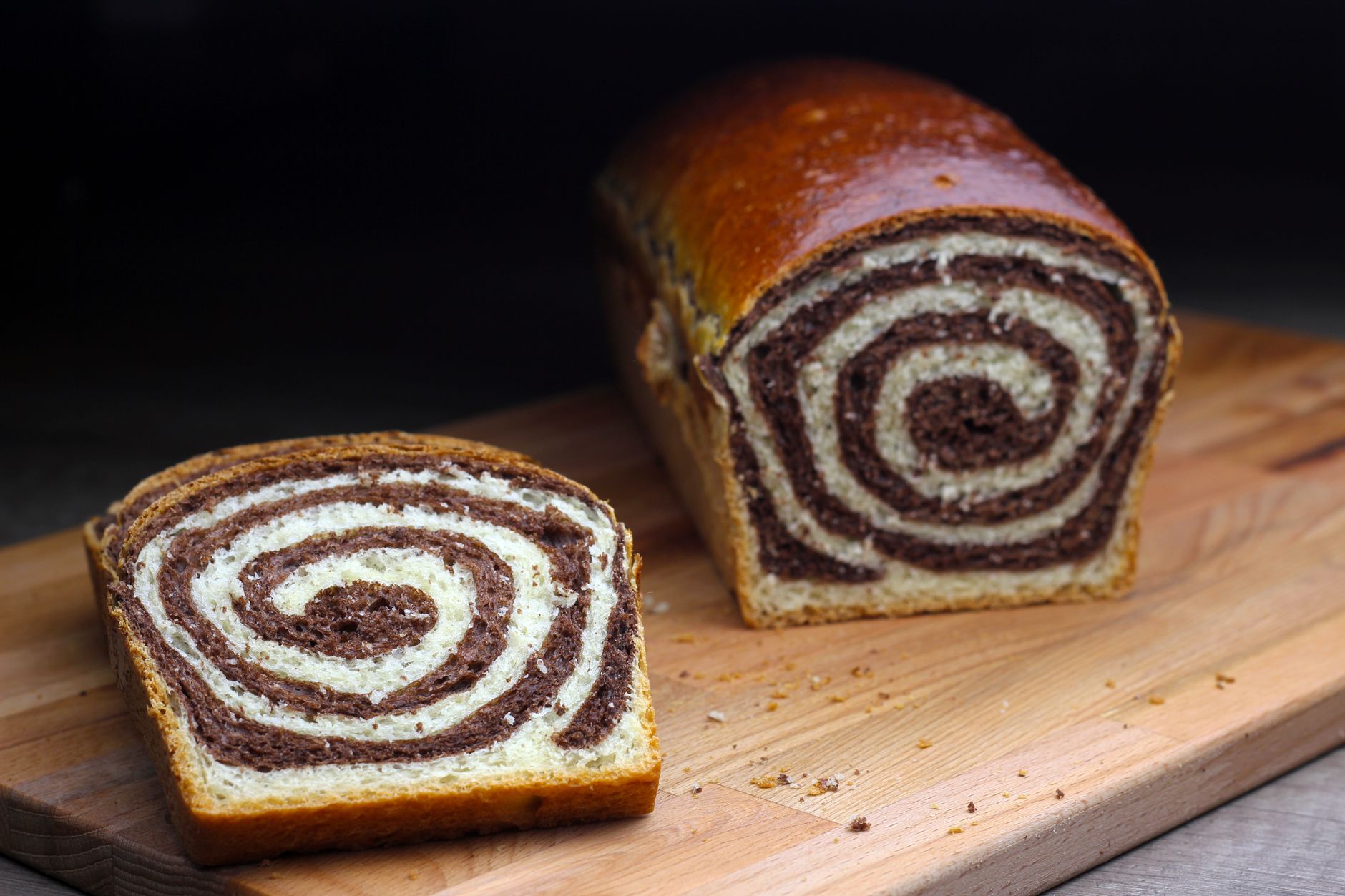 Close-up of a freshly baked swirl bread loaf and slice on a wooden cutting board