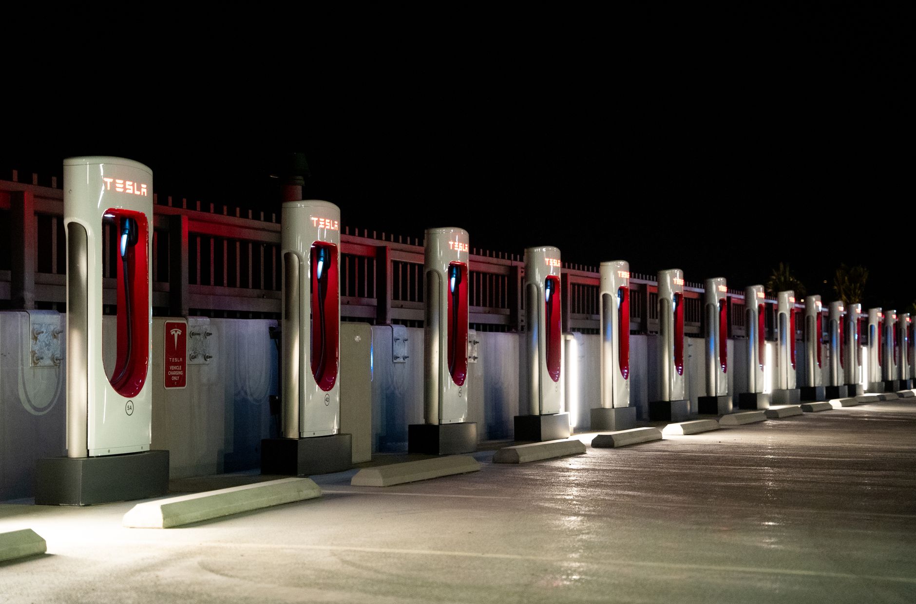 Row of Tesla Supercharger stations illuminated at night, open 24 hours