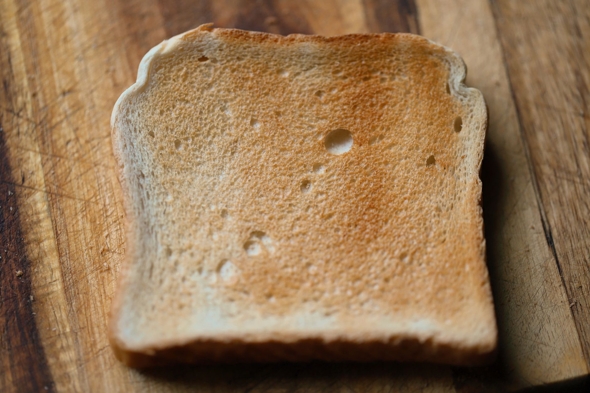 A detailed view of a single slice of toasted white bread on a wooden surface