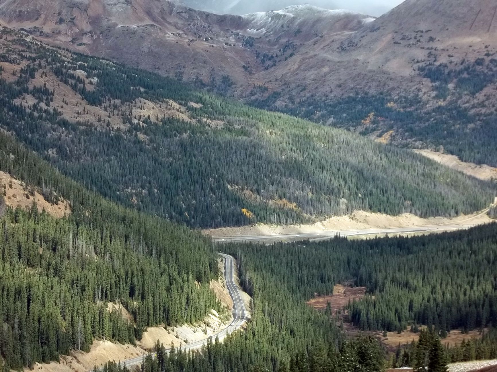 Aerial view of a highway winding through a pine forest between Colorado mountain peaks