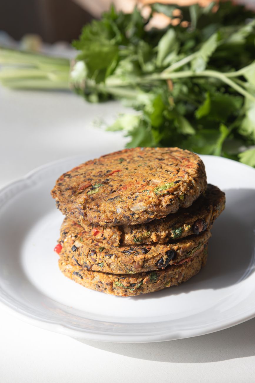 Stack of homemade vegetarian burger patties on a plate with fresh herbs