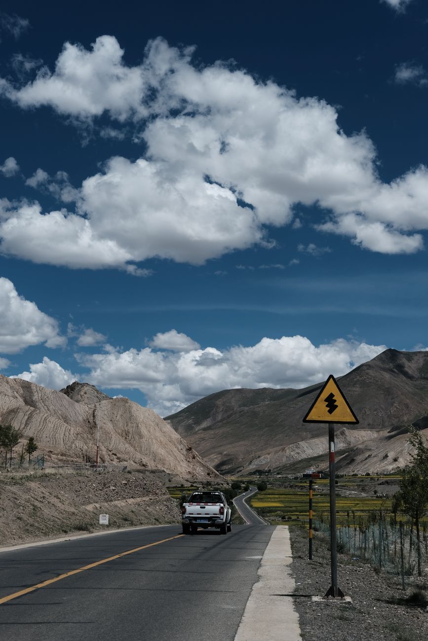 A vehicle travels a mountain highway under a dramatic sky