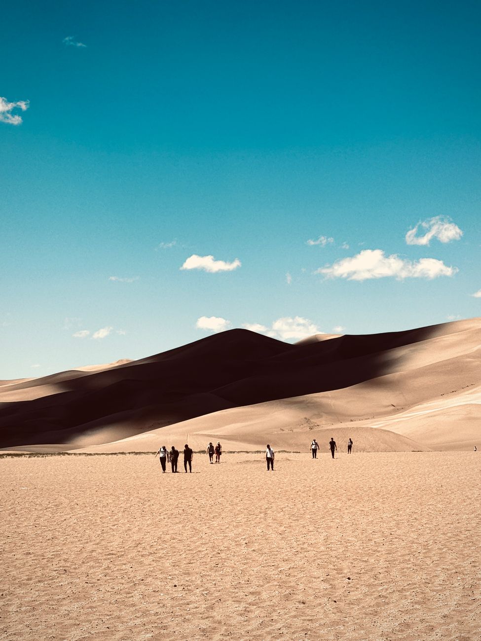 Visitors exploring the vast, sunlit sand dunes under a clear blue sky
