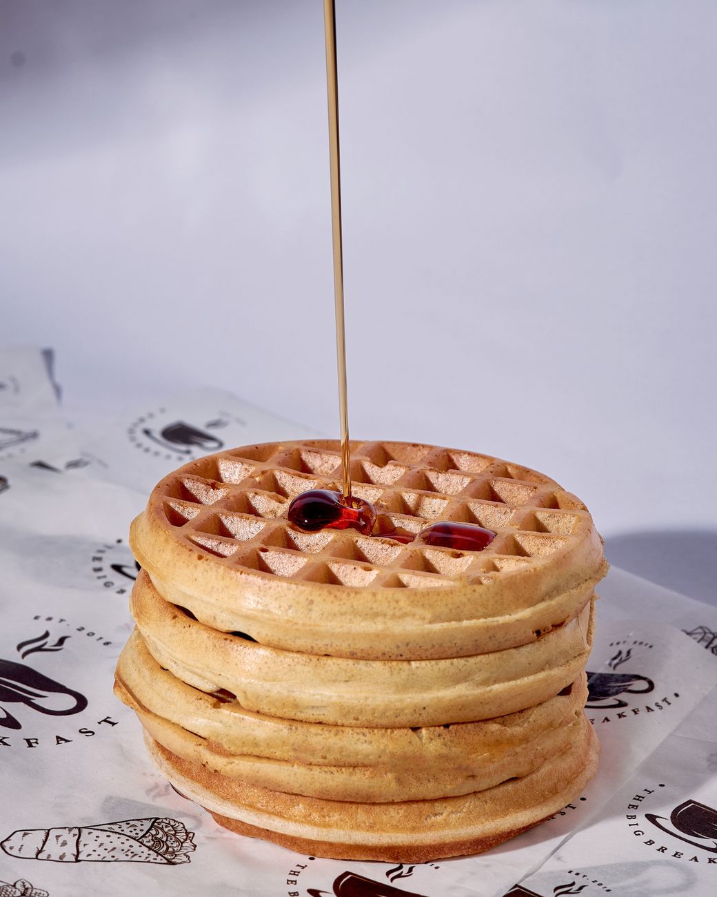 A stack of waffles with syrup drizzling down the sides