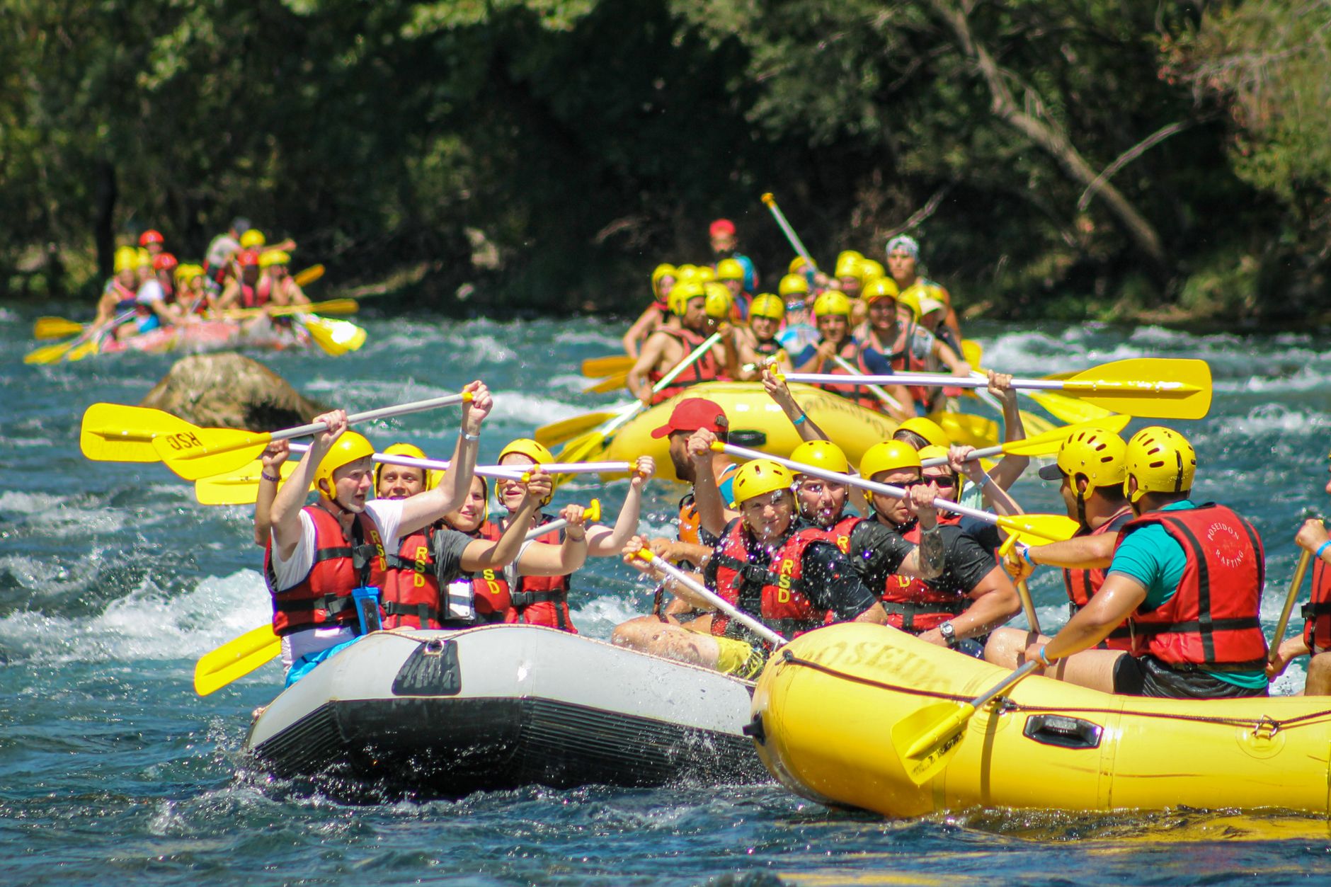 Teams of rafters navigating rapids in colorful inflatable boats on a river