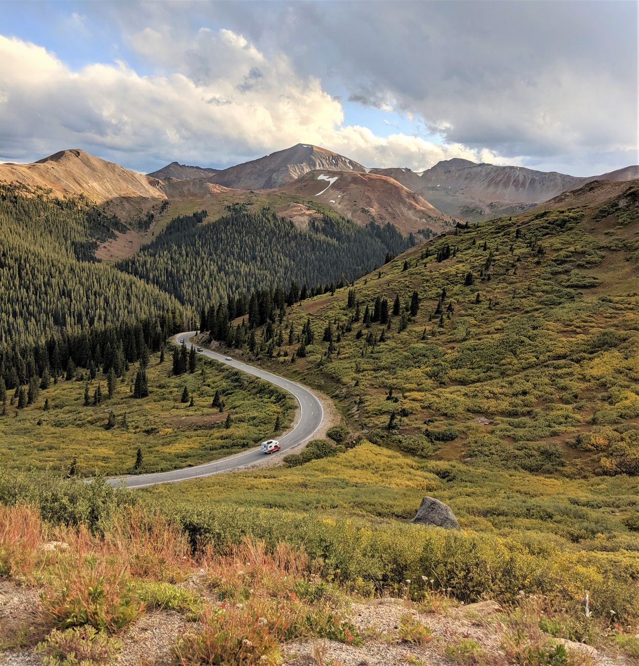 Curvy two-lane mountain road winding through a forested Colorado valley