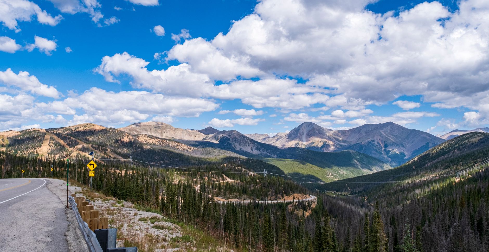 Panoramic view of a winding road through the Rocky Mountains under a blue sky