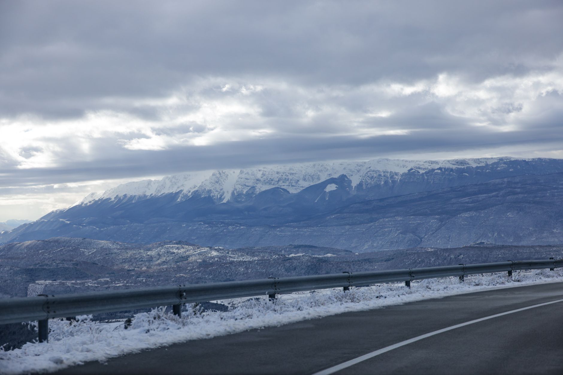 Two-lane mountain road winding through snow under a cloudy Colorado sky