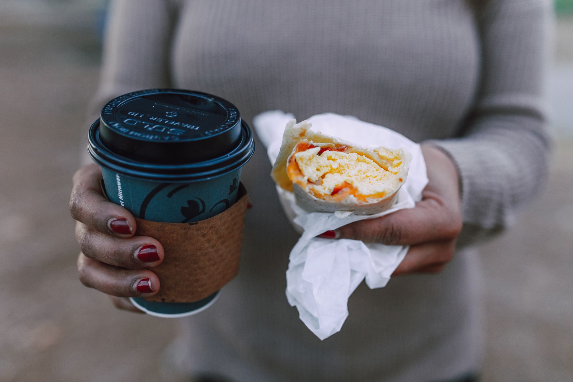 A woman holding a hot coffee cup and a breakfast sandwich